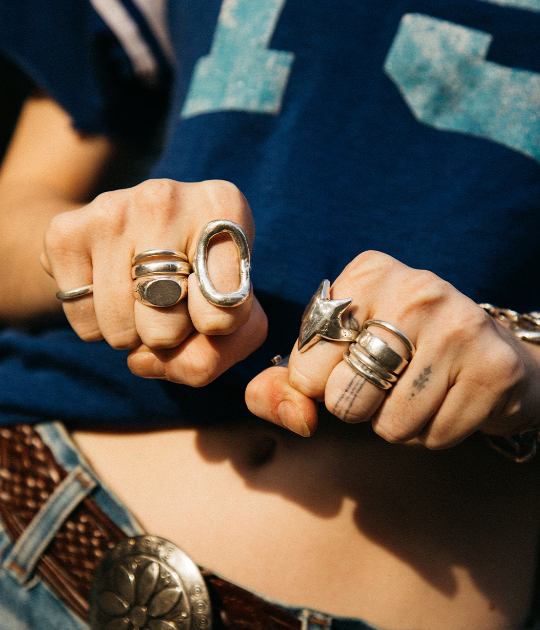 Close-up of hands with multiple rings on fingers, wearing a blue denim jacket.