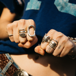 Close-up of hands with multiple rings on fingers, wearing a blue denim jacket.