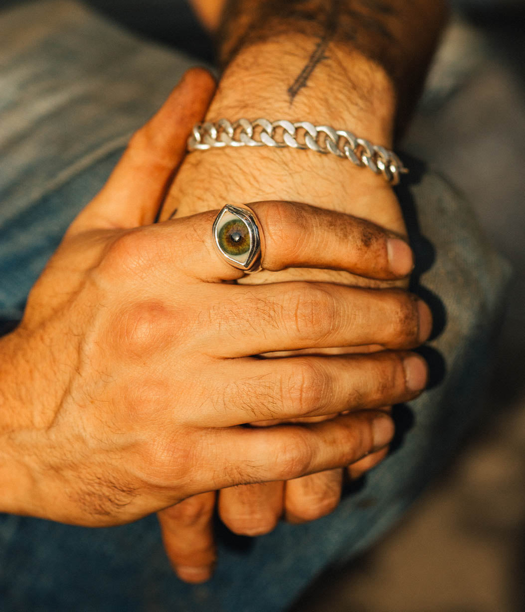 Close-up of a hand with a silver chain bracelet and a ring, against a blurred background.