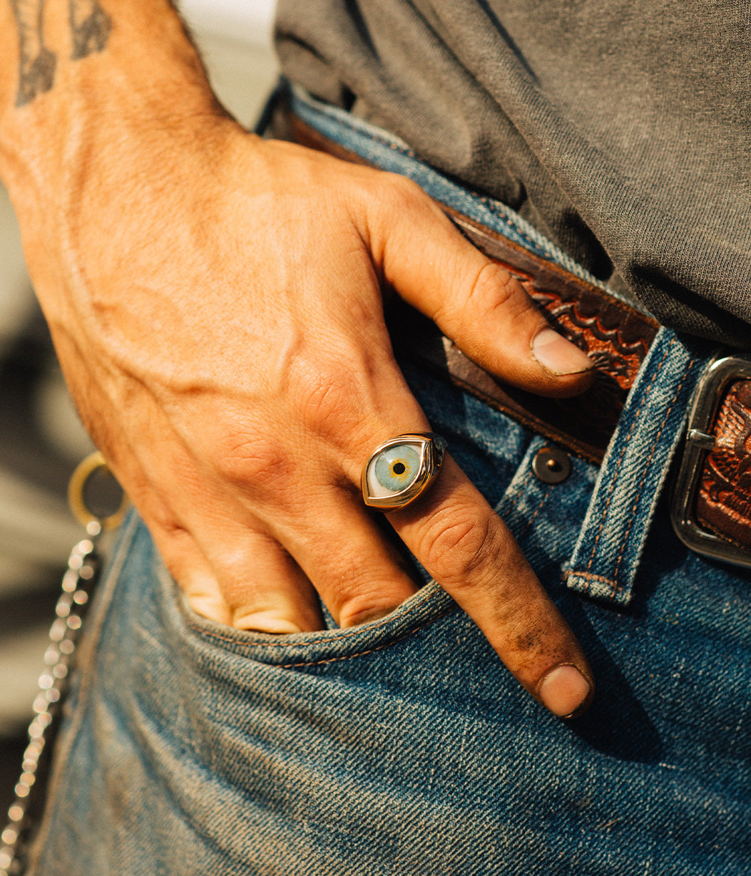 Hand wearing a ring with an eye design, holding a chain, against a blurred background.