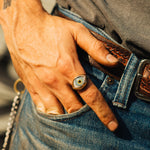 Hand wearing a ring with an eye design, holding a chain, against a blurred background.