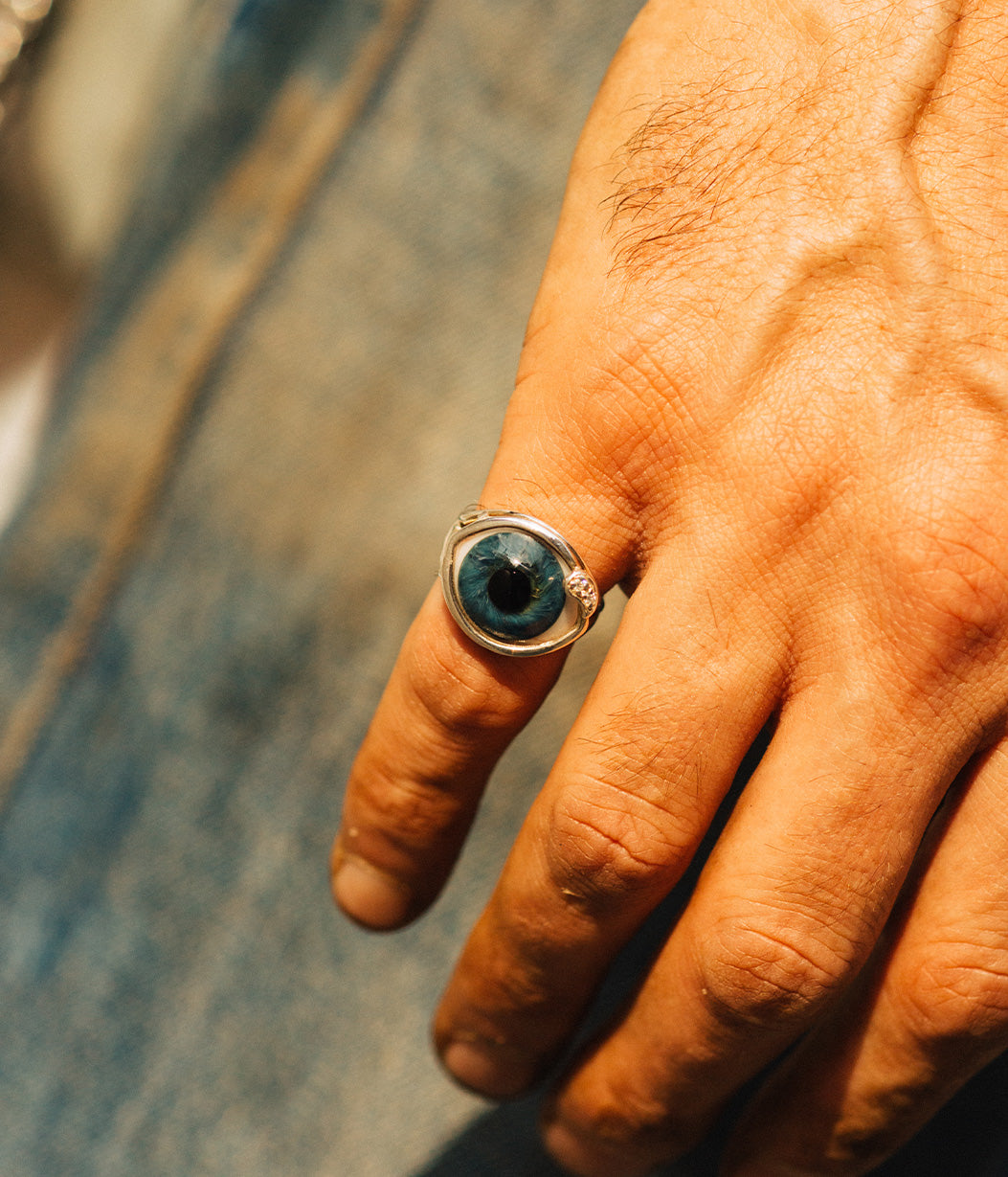 Hand wearing a ring with a blue gemstone on a blurred background
