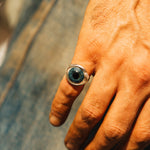 Hand wearing a ring with a blue gemstone on a blurred background