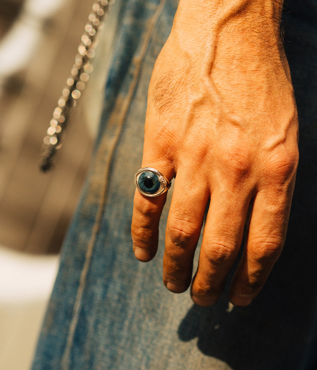 Hand wearing a ring with a blue stone against a blurred background