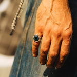 Hand wearing a ring with a blue stone against a blurred background