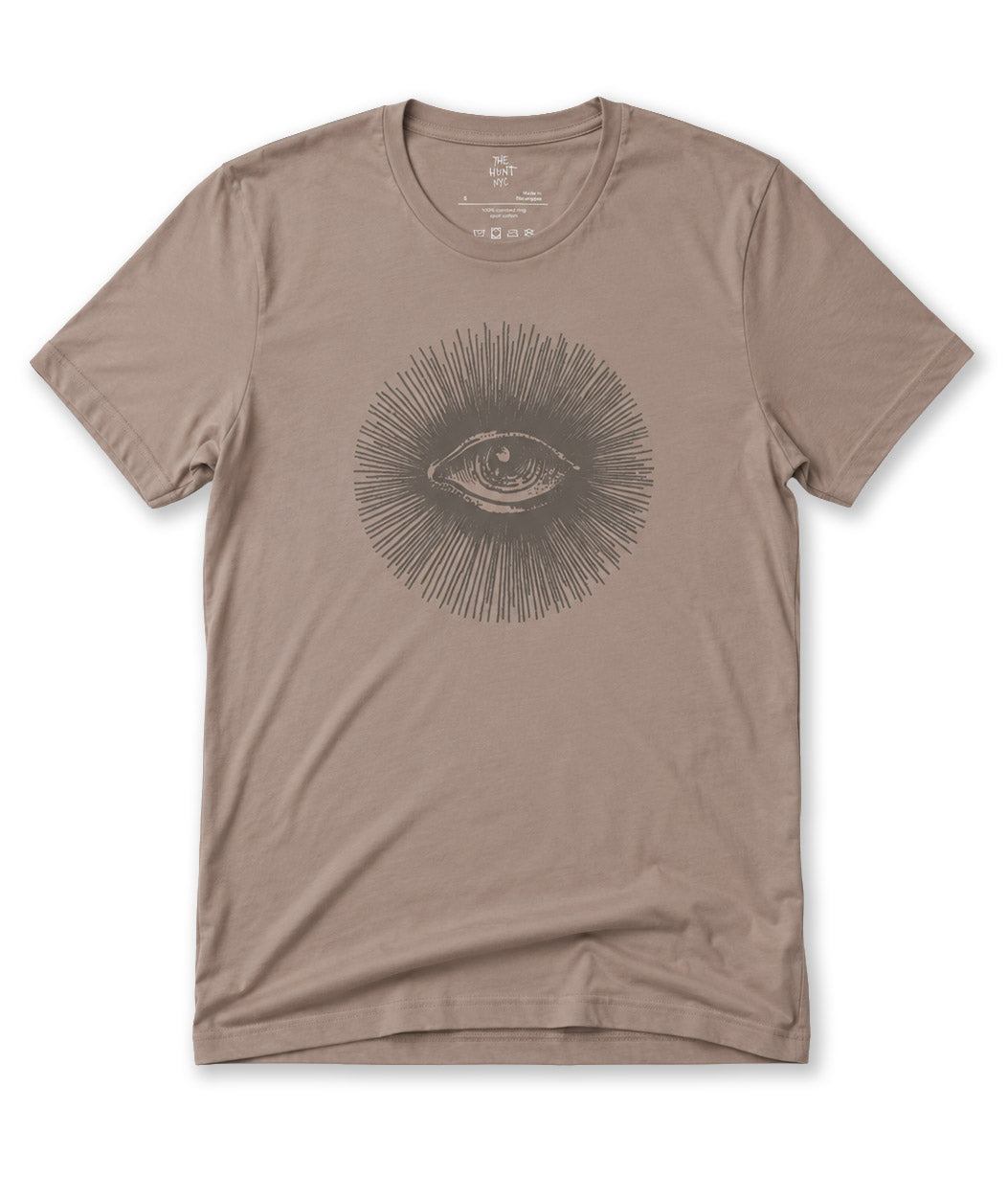 A taupe brown short-sleeve crewneck t-shirt featuring a dark gray line art graphic of an eye surrounded by radiating lines on the chest, displayed flat against a white background.