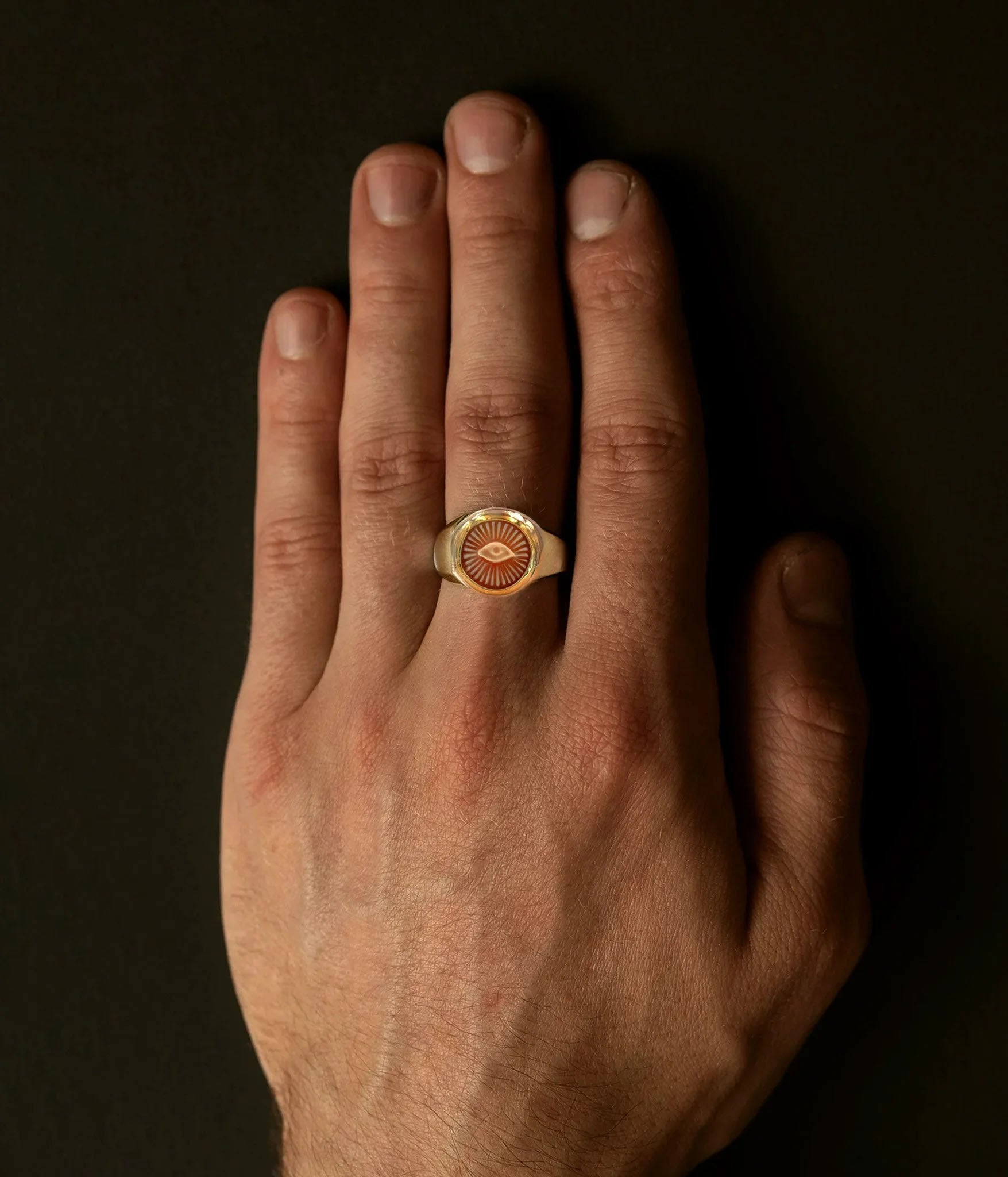 Hand wearing a gold ring with an eye design on a dark background