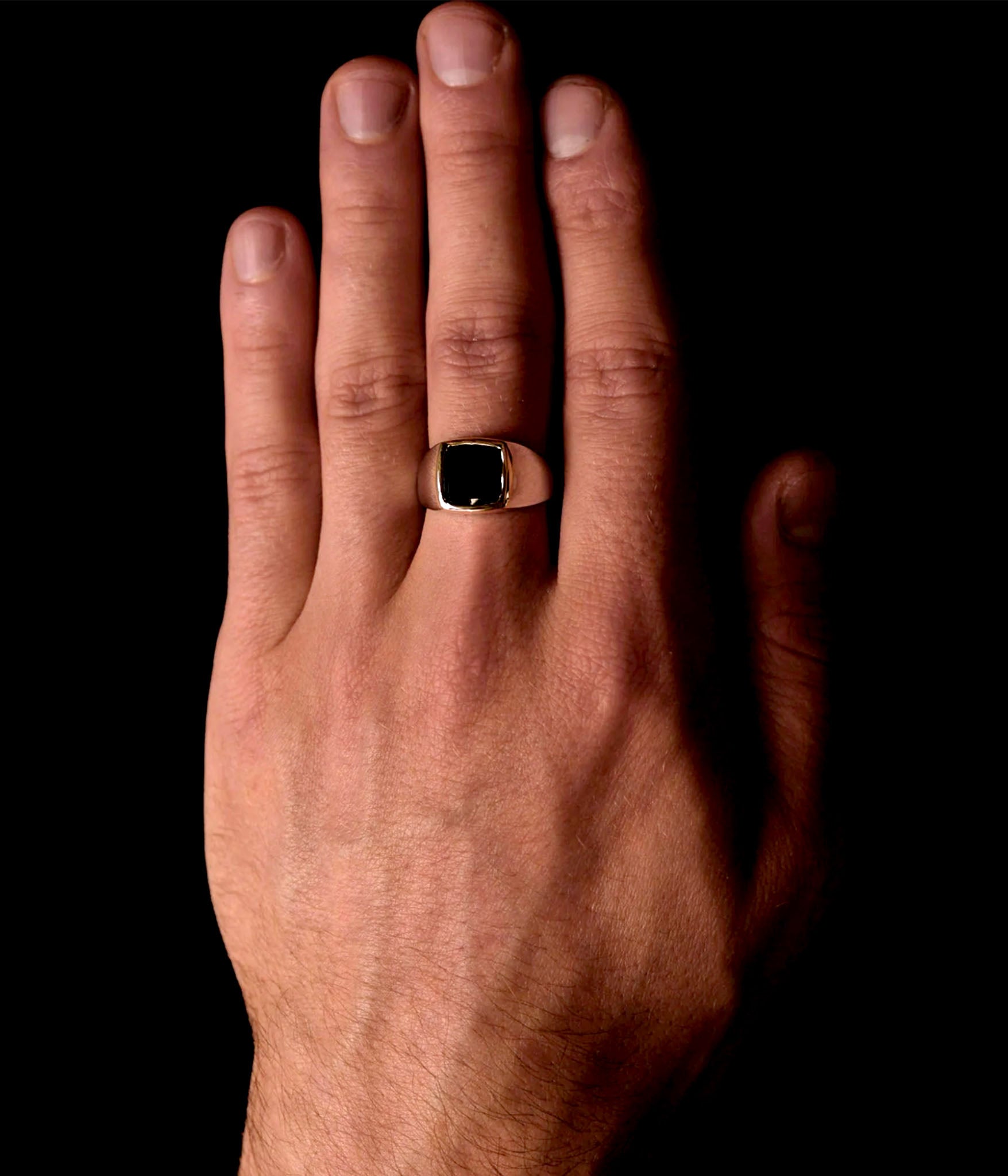 Hand wearing a gold ring with a black gemstone on a black background