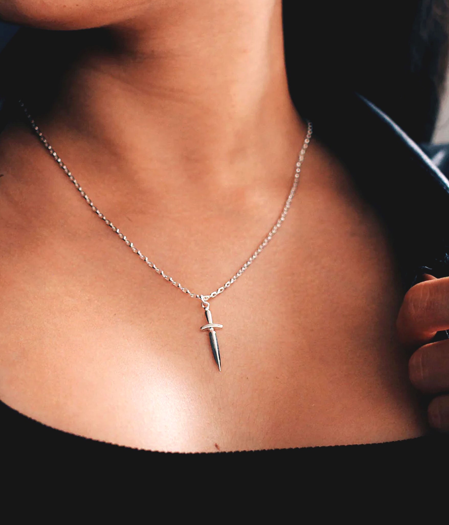 Sterling silver dagger necklace worn on model – minimalist blade pendant resting on chest, styled with black outfit for edgy look