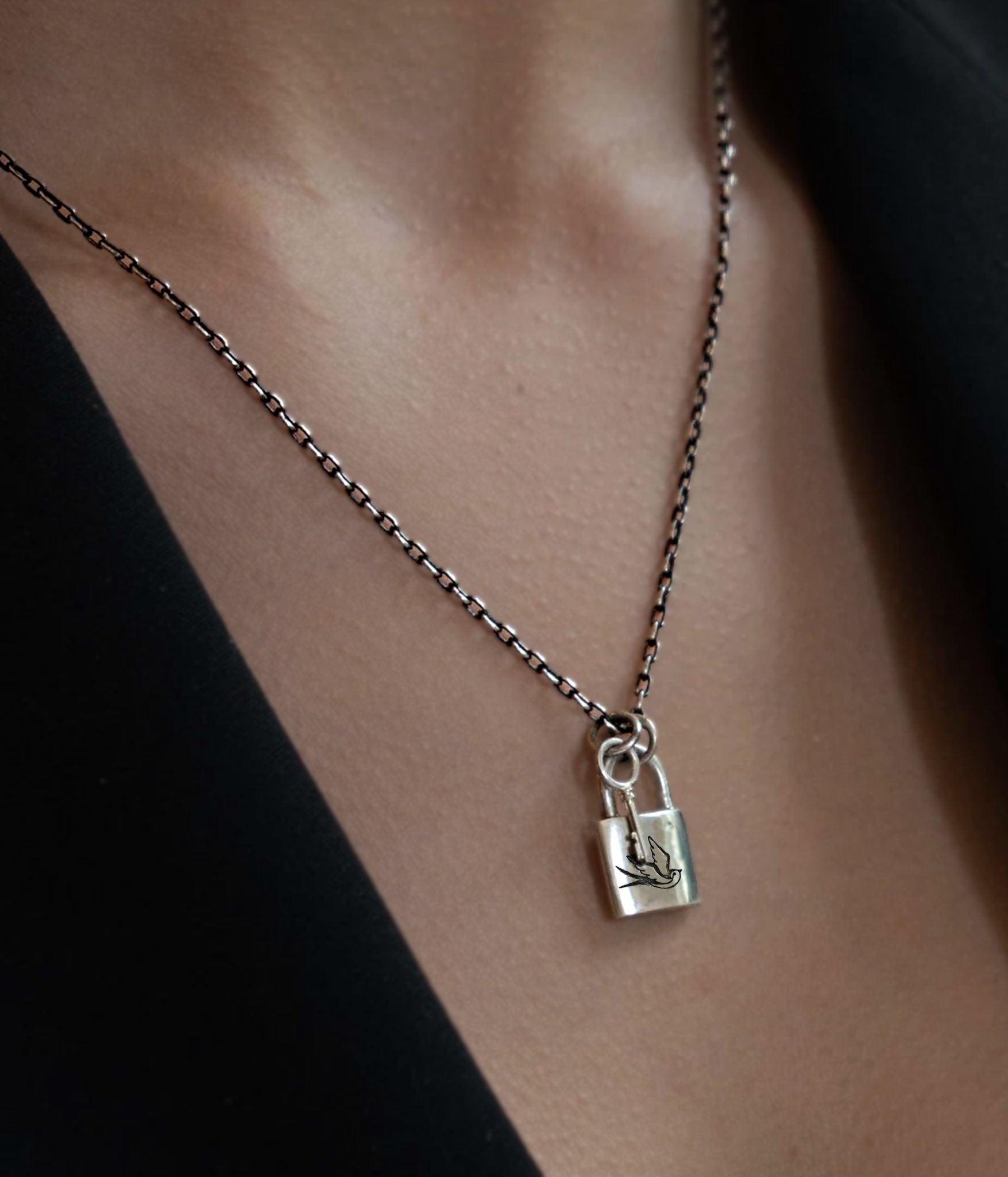 Model wearing swallow-engraved silver lock and key necklace on black chain, minimal styling