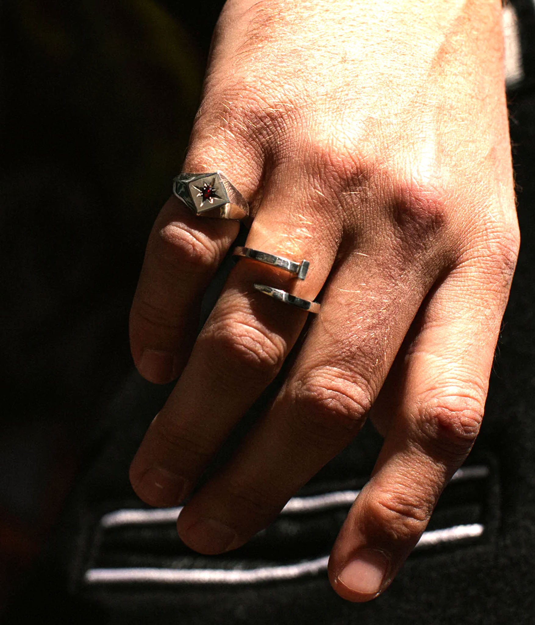 Editorial close-up of a hand wearing The Hunt’s Tough as Nails ring in sterling silver. Twisted nail form wraps the finger with raw, sculptural intent. Harsh directional lighting and shadow.