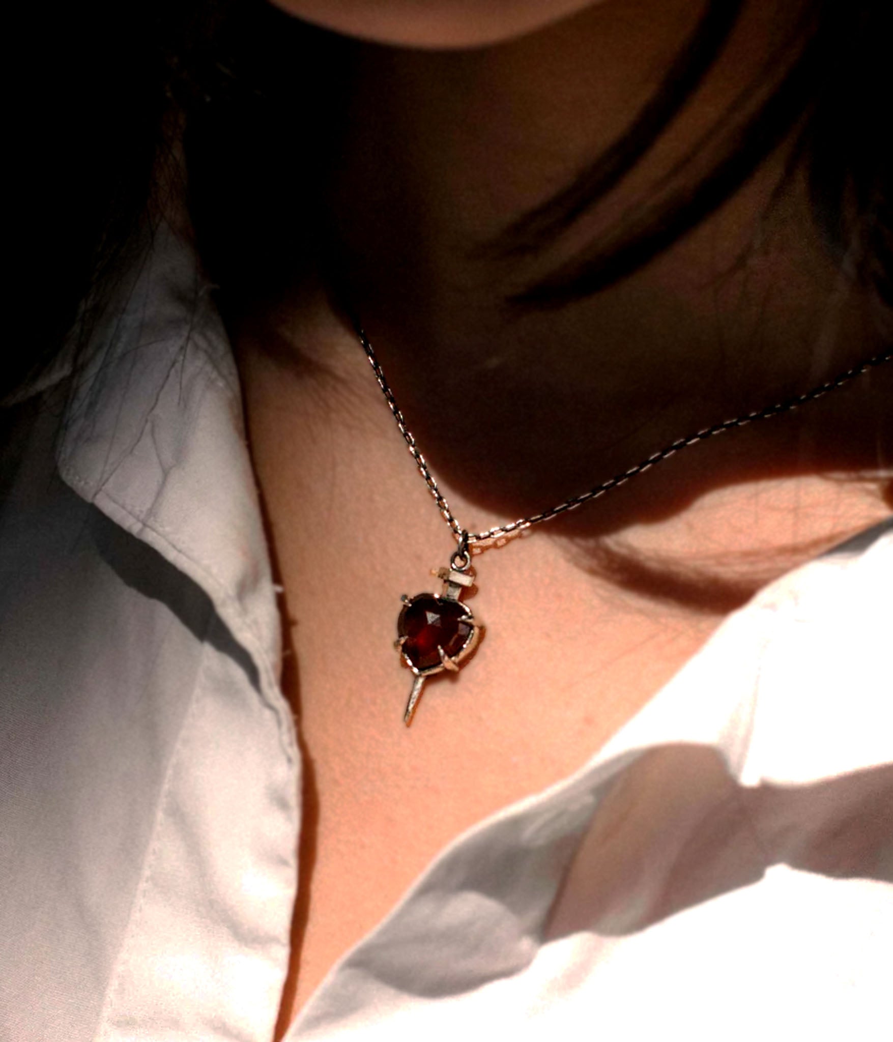 Nail through the heart garnet necklace worn on model with white shirt, gothic romantic jewelry look