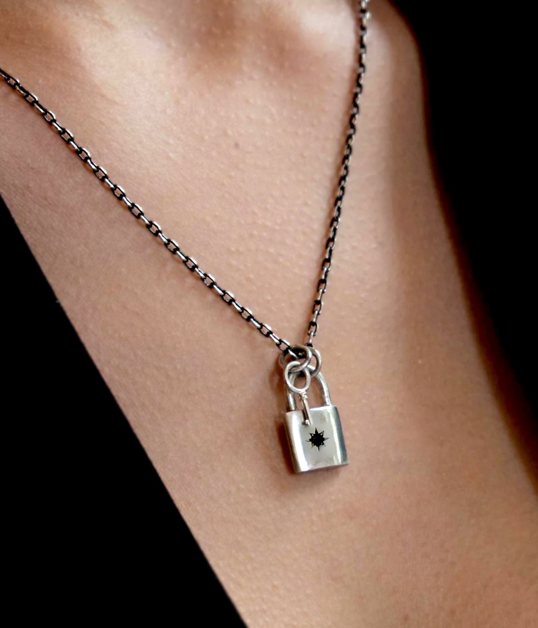 Padlock and key necklace worn on model – sterling silver charm necklace with blackened chain and star-set gemstone detail.