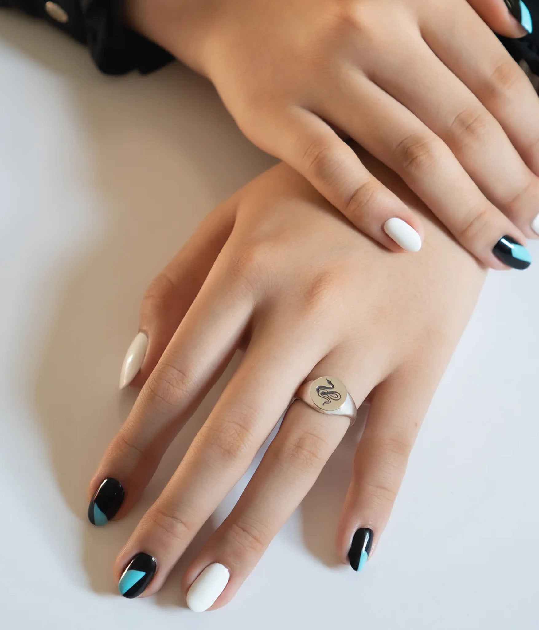 Traditional round sterling silver signet ring with snake engraving by Futaba for The Hunt on females hand with painted nails in soft light
