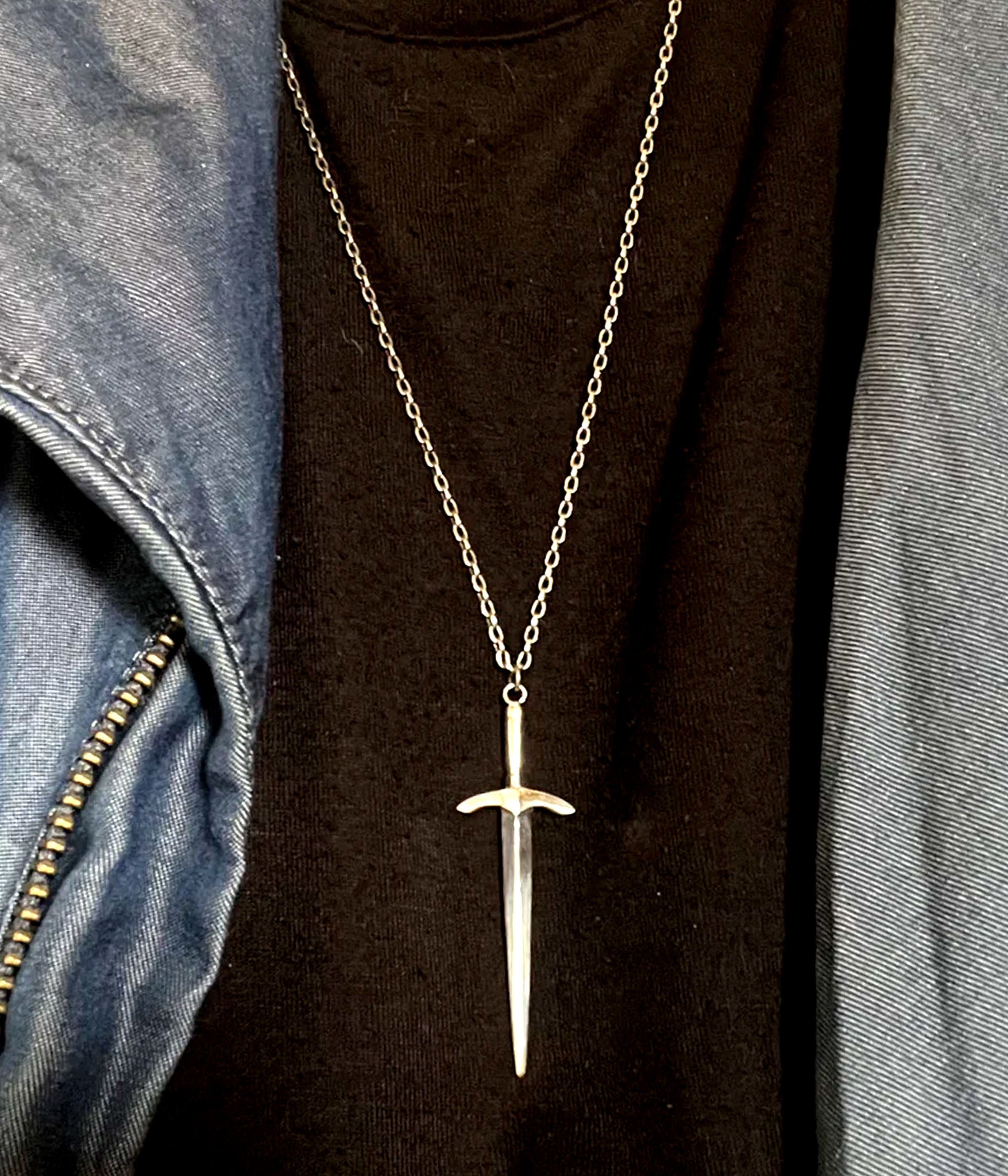 Sterling silver sword pendant necklace by The Hunt – worn over black shirt with long silver chain and minimalist dagger charm