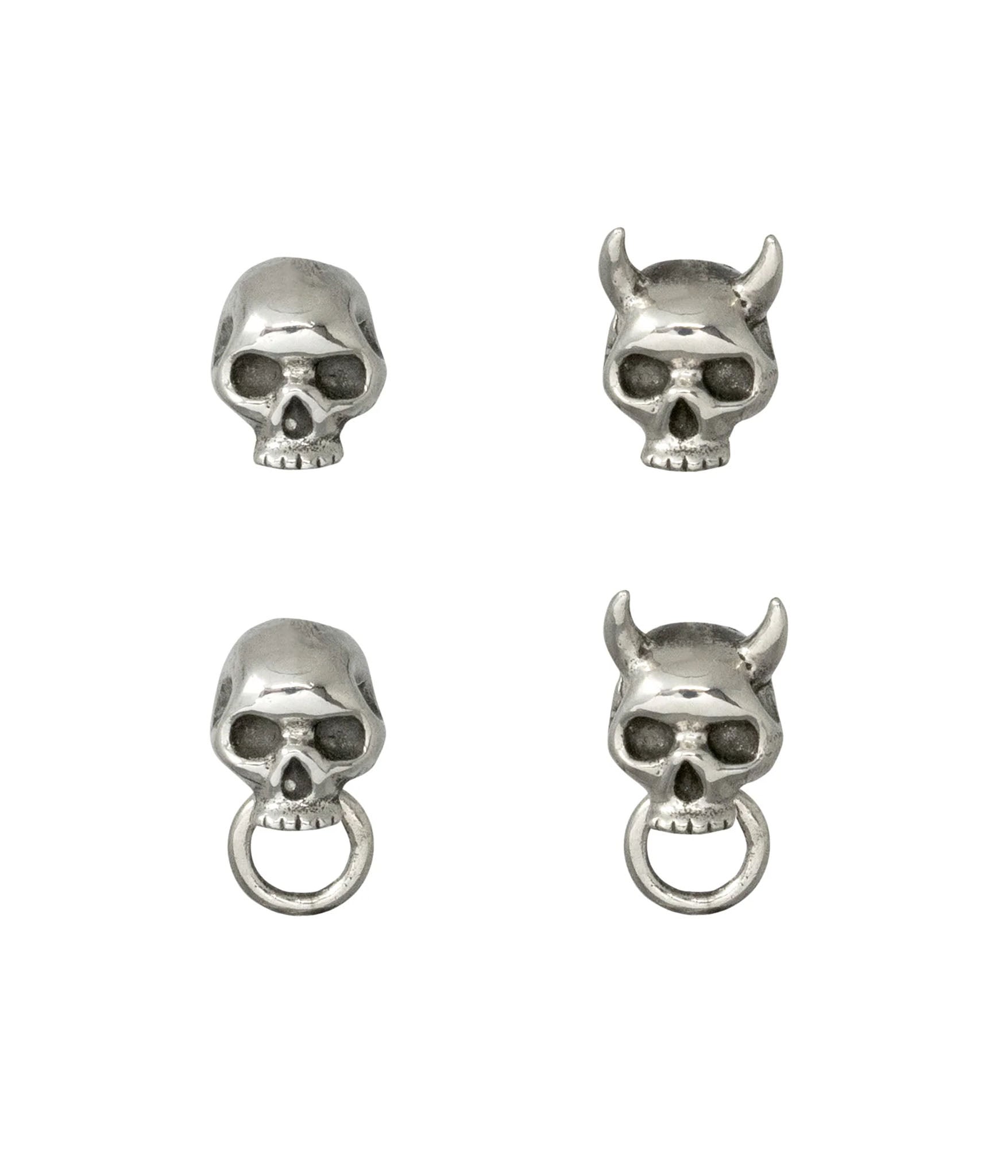 Flat lay of four sterling silver skull stud earrings in varying styles: classic skull, horned Oni skull, skull with ring, and horned Oni skull with ring. 