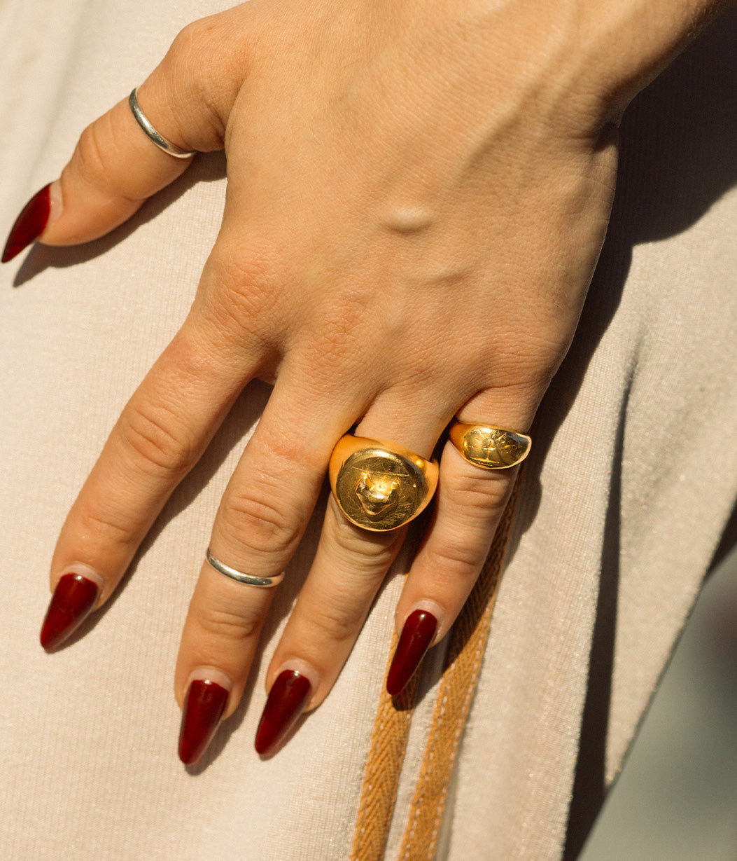 Hand with gold rings and red nail polish on a neutral background