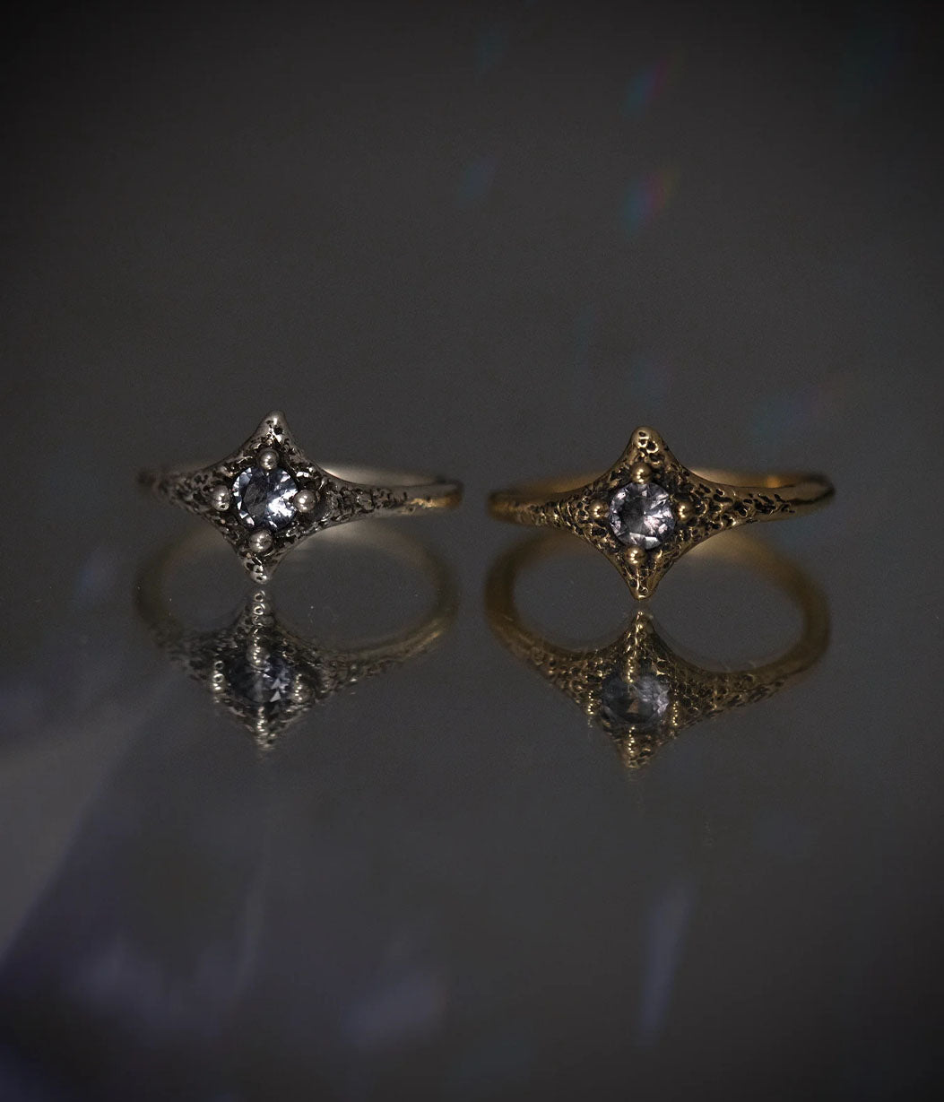 Two gold rings with gemstones on a reflective surface