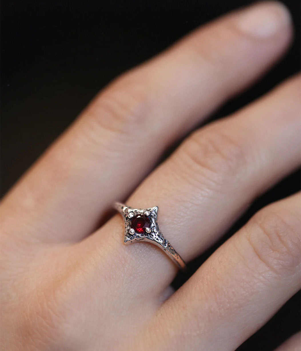 Rose gold ring with a red gemstone on a finger against a dark background