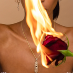 Person holding a flaming red rose with a necklace featuring a pendant.