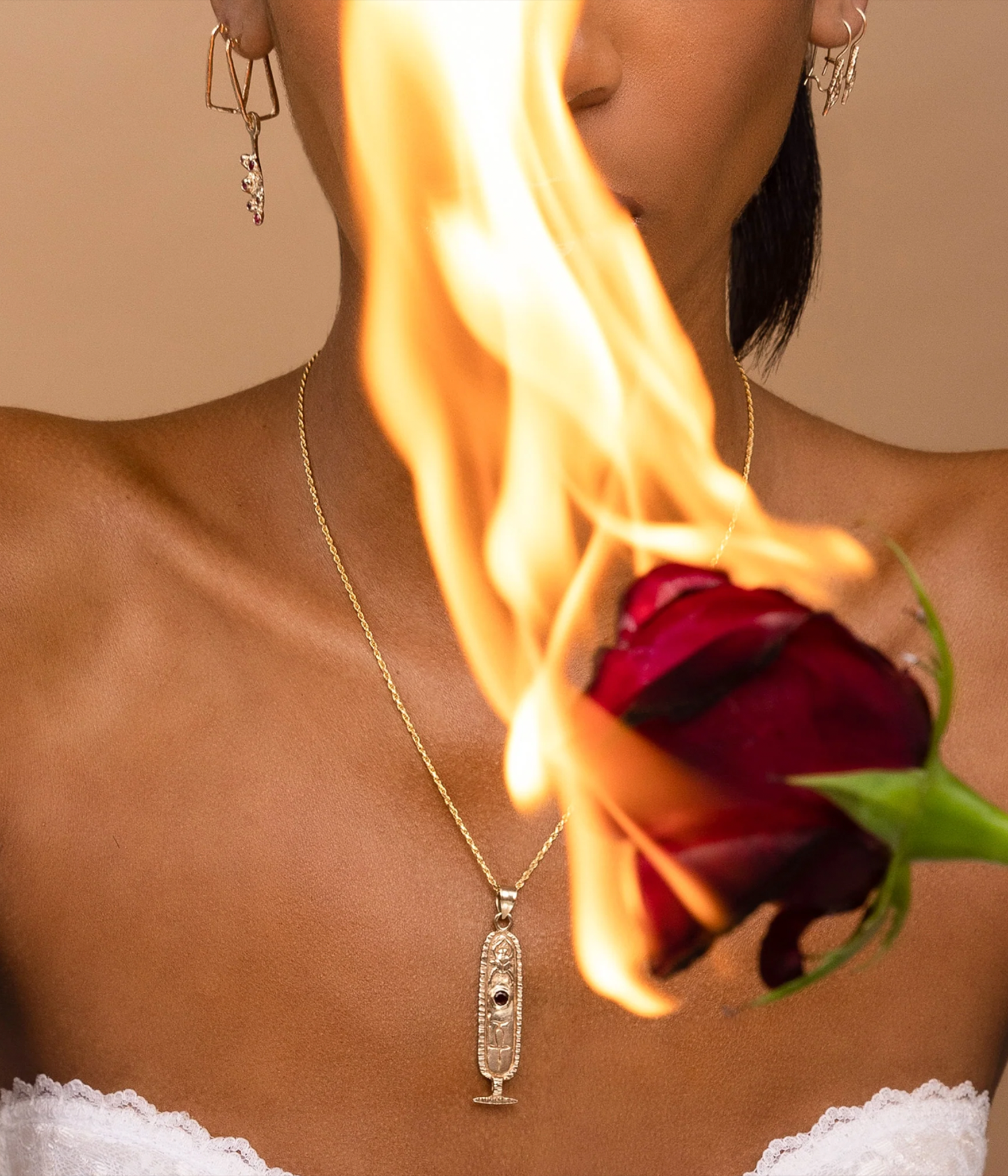 Person holding a flaming red rose with a necklace featuring a pendant.
