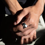 Close-up of a hand wearing a silver ring with a dark background