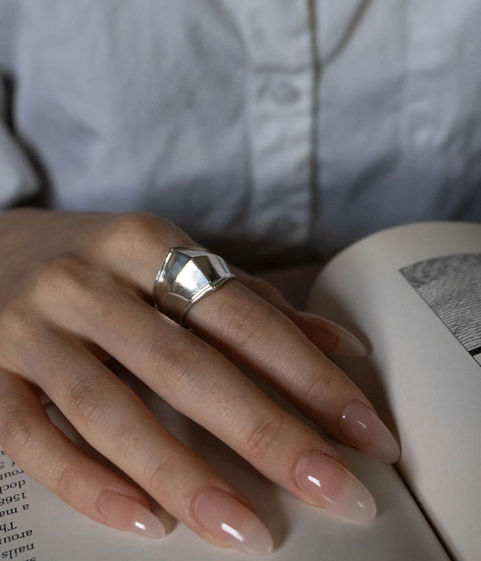 Hand wearing a silver ring on an open book with a blurred background
