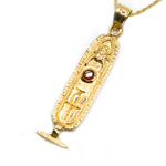 Gold pendant with a red gemstone on a white background