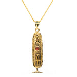 Gold pendant necklace with a central red gemstone on a white background