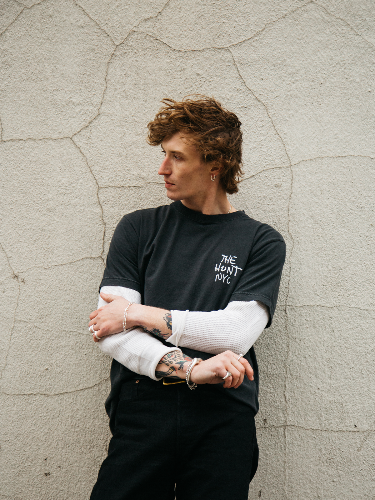 Person wearing a black sweatshirt with text, standing against a textured wall.