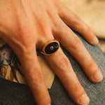 Hand wearing a gold ring with a dark stone on a textured surface