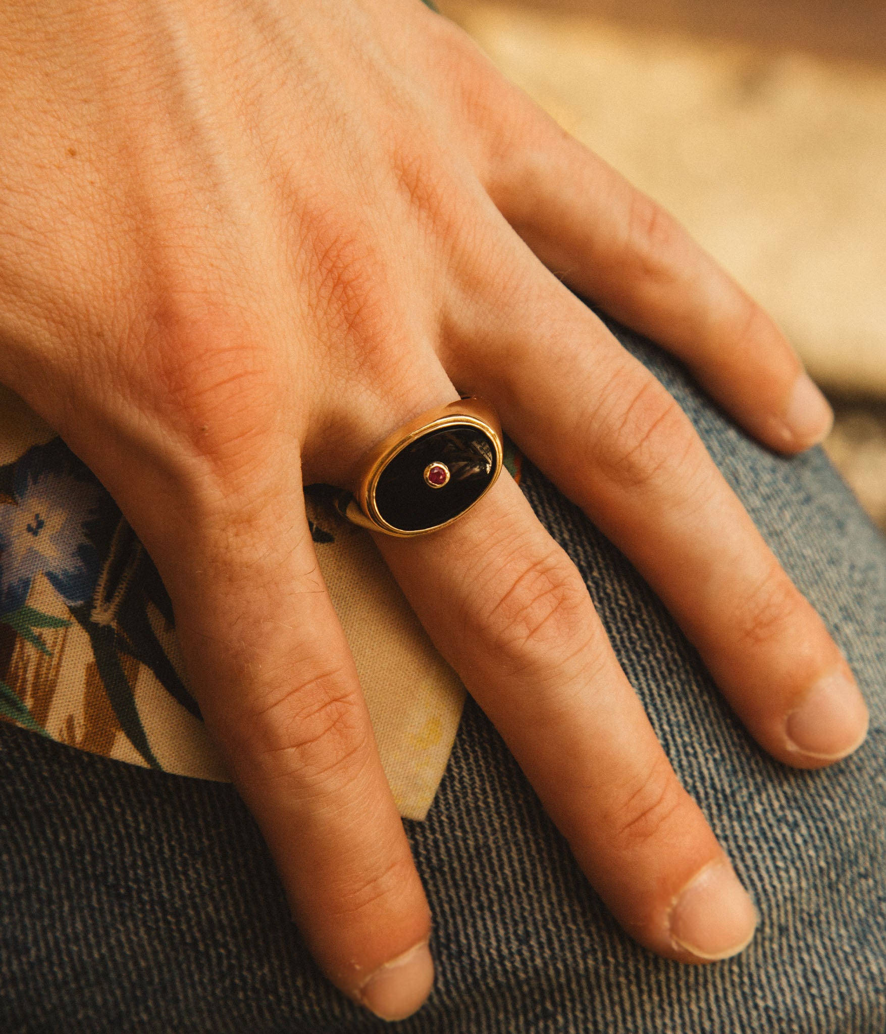 Hand wearing a gold ring with a dark stone on a textured surface