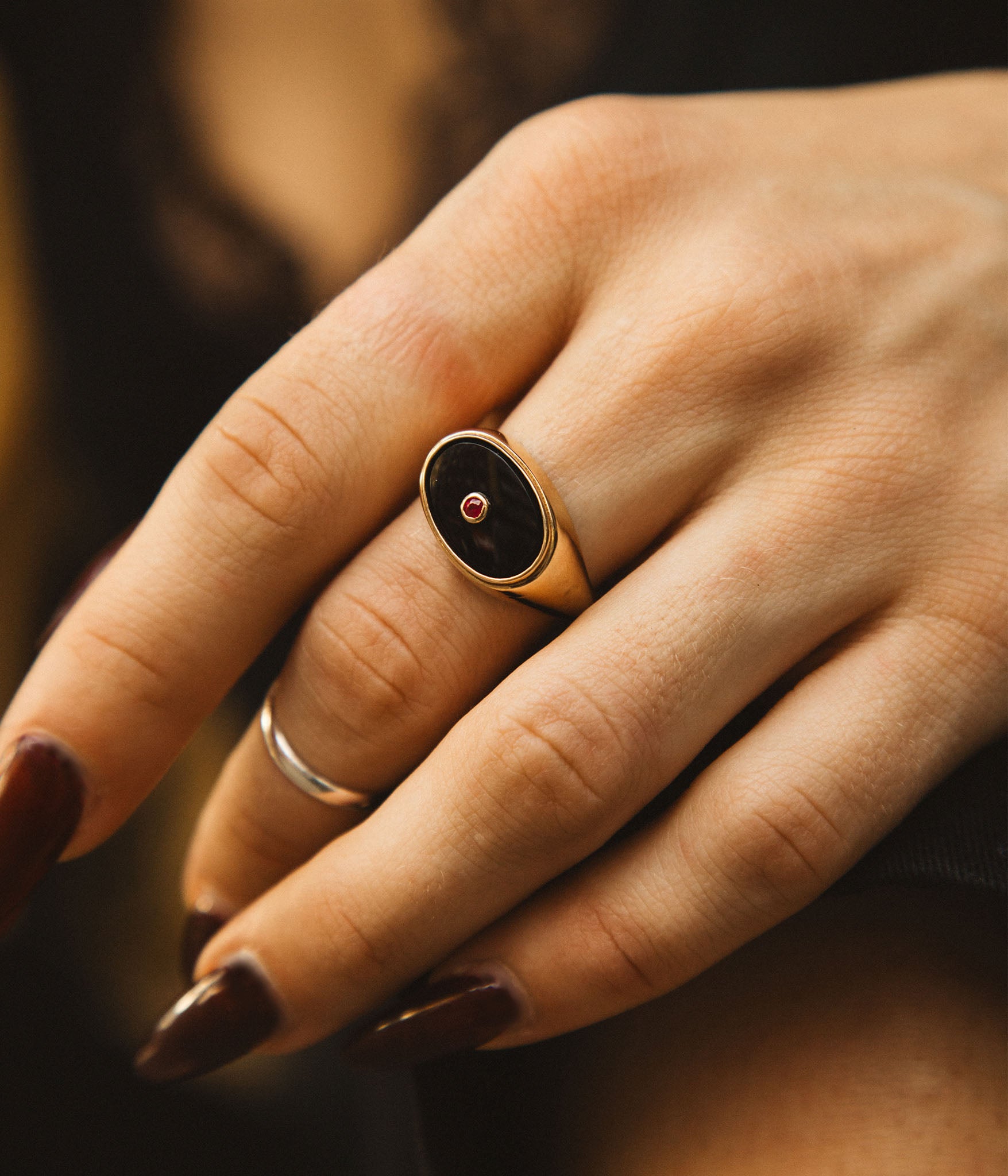 Close-up of a hand wearing a gold ring with a dark stone on a blurred background