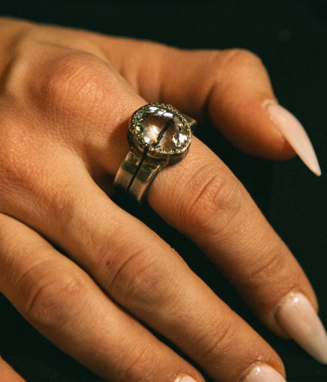 Close-up of a hand wearing a silver ring with a large gemstone on a dark background
