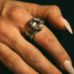 Close-up of a hand wearing a silver ring with a large gemstone on a dark background