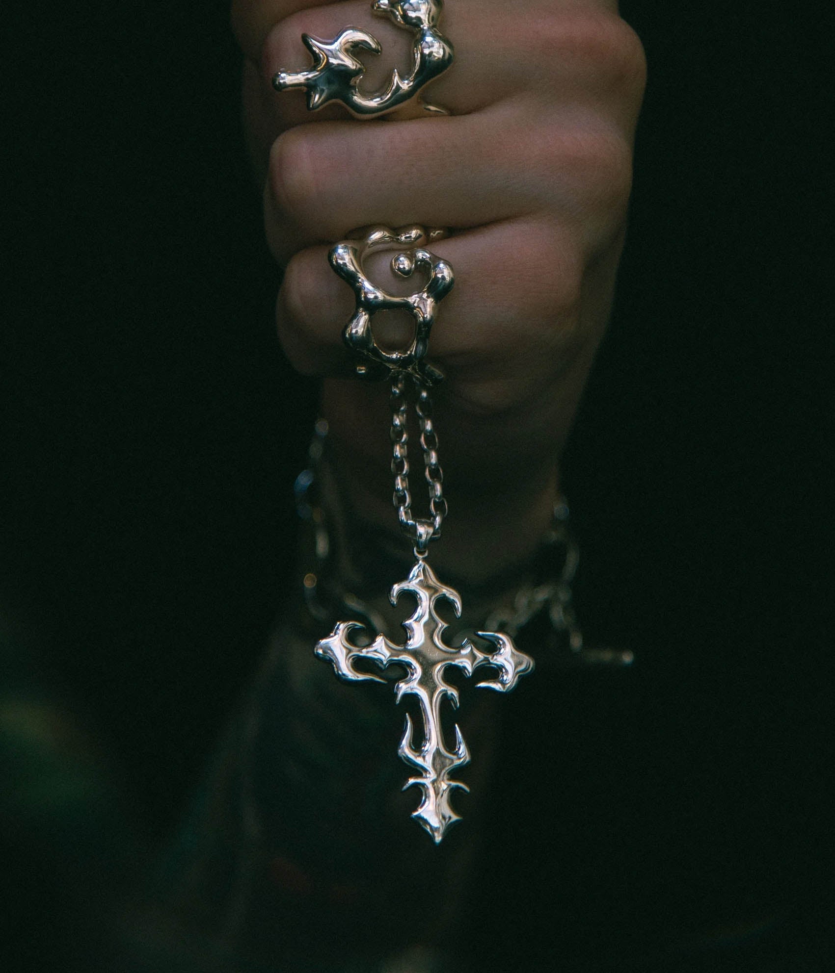 Hand wearing multiple silver rings with intricate designs on a dark background