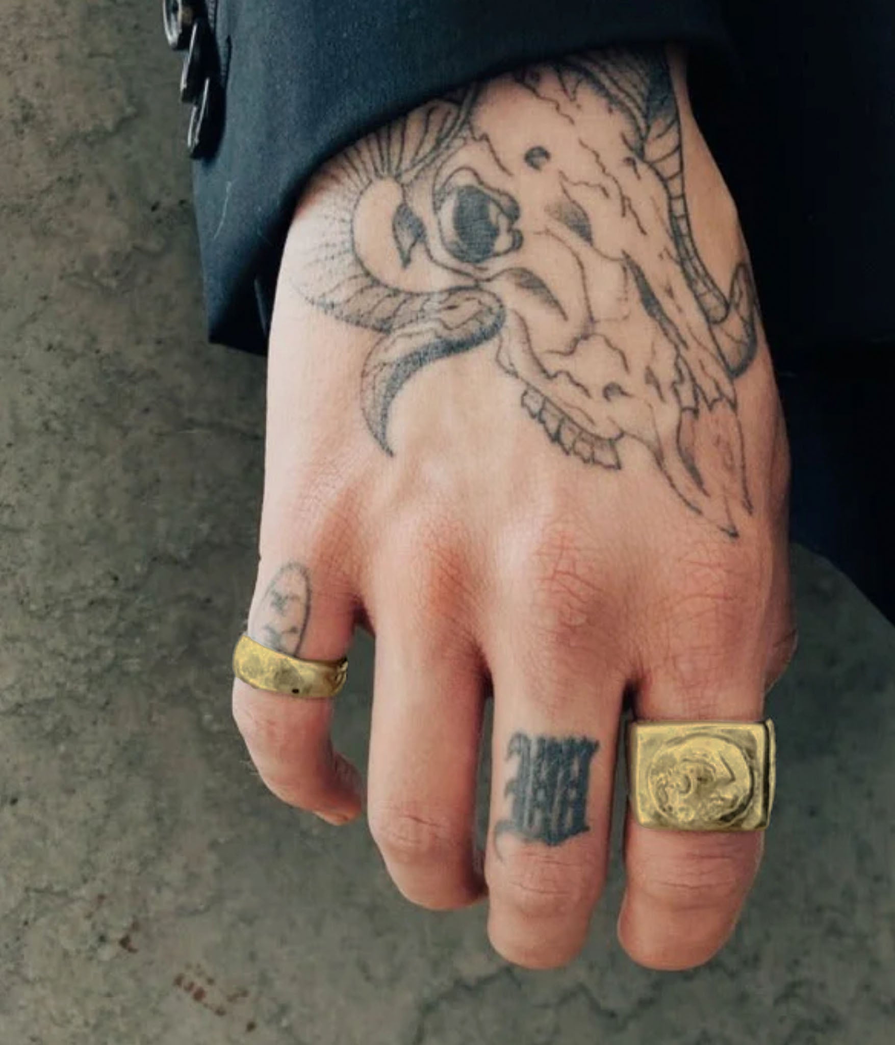 Hand with tattoos and gold rings against a concrete wall