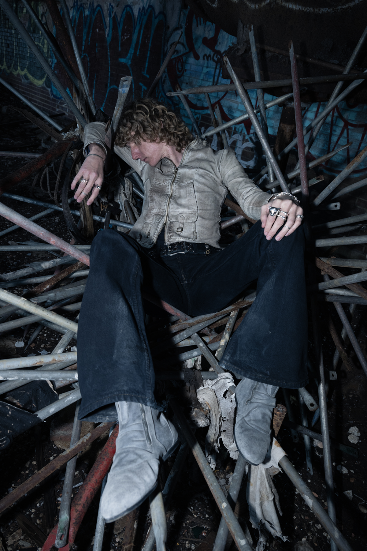 Person sitting on a pile of metal rods with a dark, industrial background