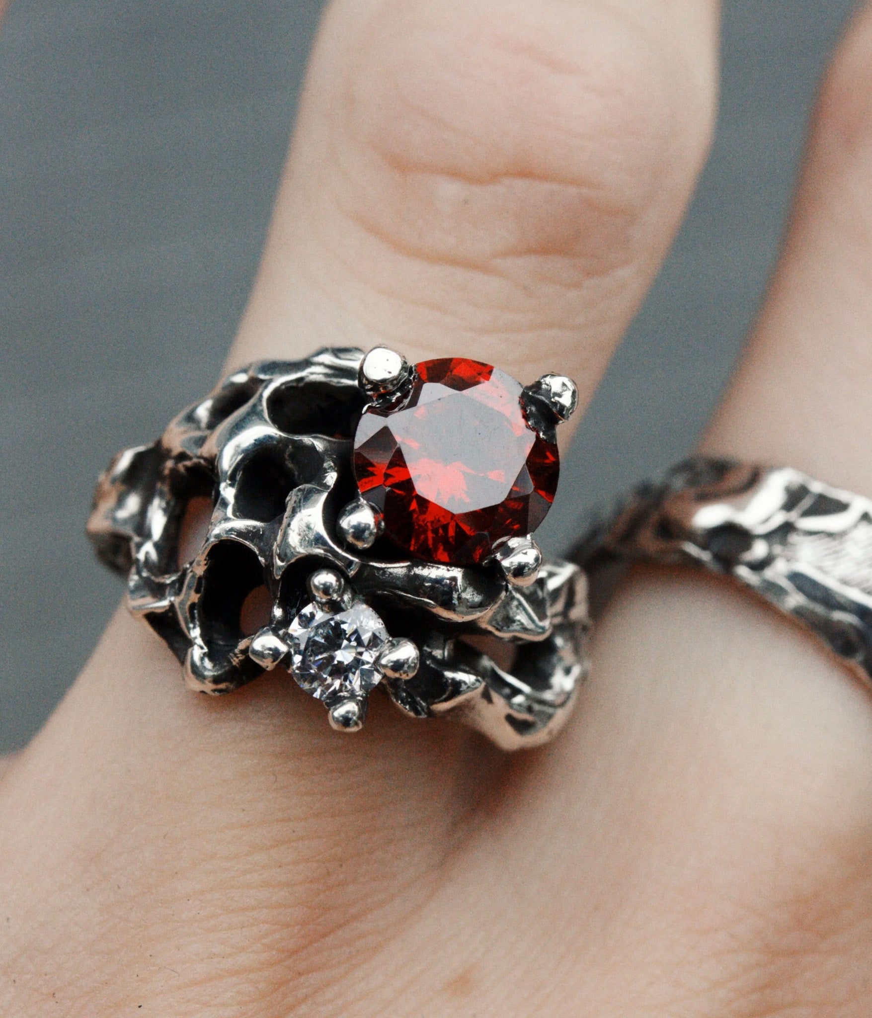 Silver ring with a red gemstone on a finger against a gray background