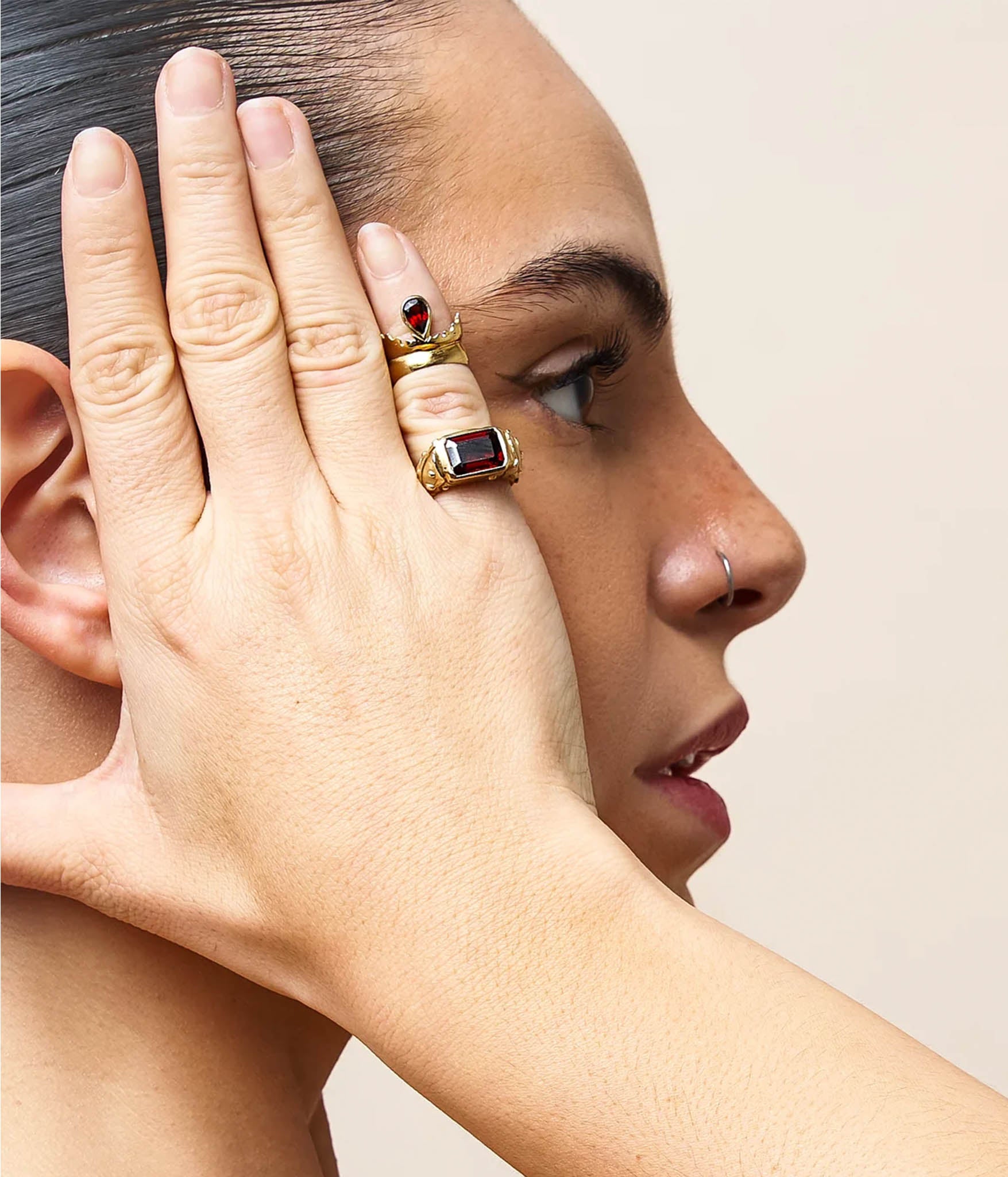 Close-up of a person wearing gold rings with gemstones on a neutral background