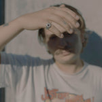 Person wearing a graphic t-shirt with text and design, holding hand up to face.