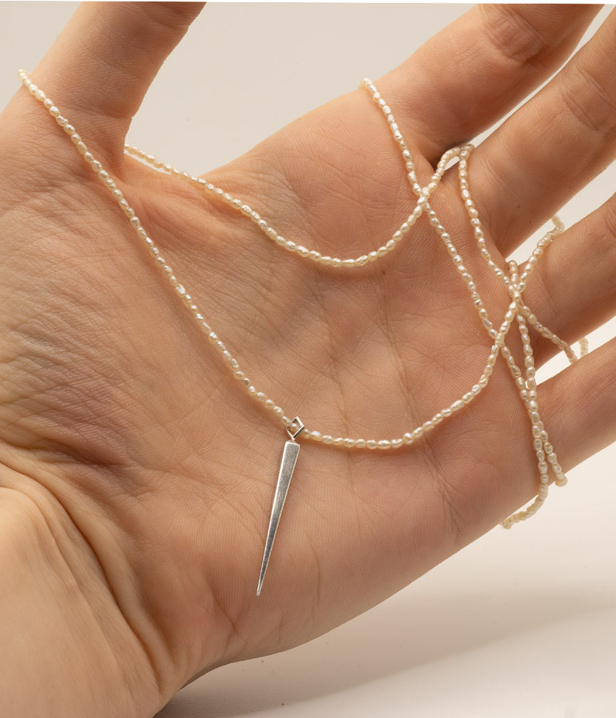 Hand holding a pearl necklace with a silver pendant against a neutral background