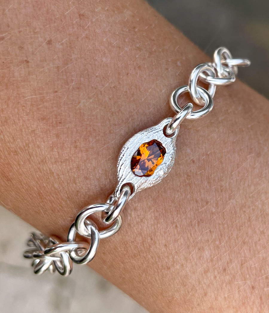 Silver bracelet with a central amber stone on a wrist.