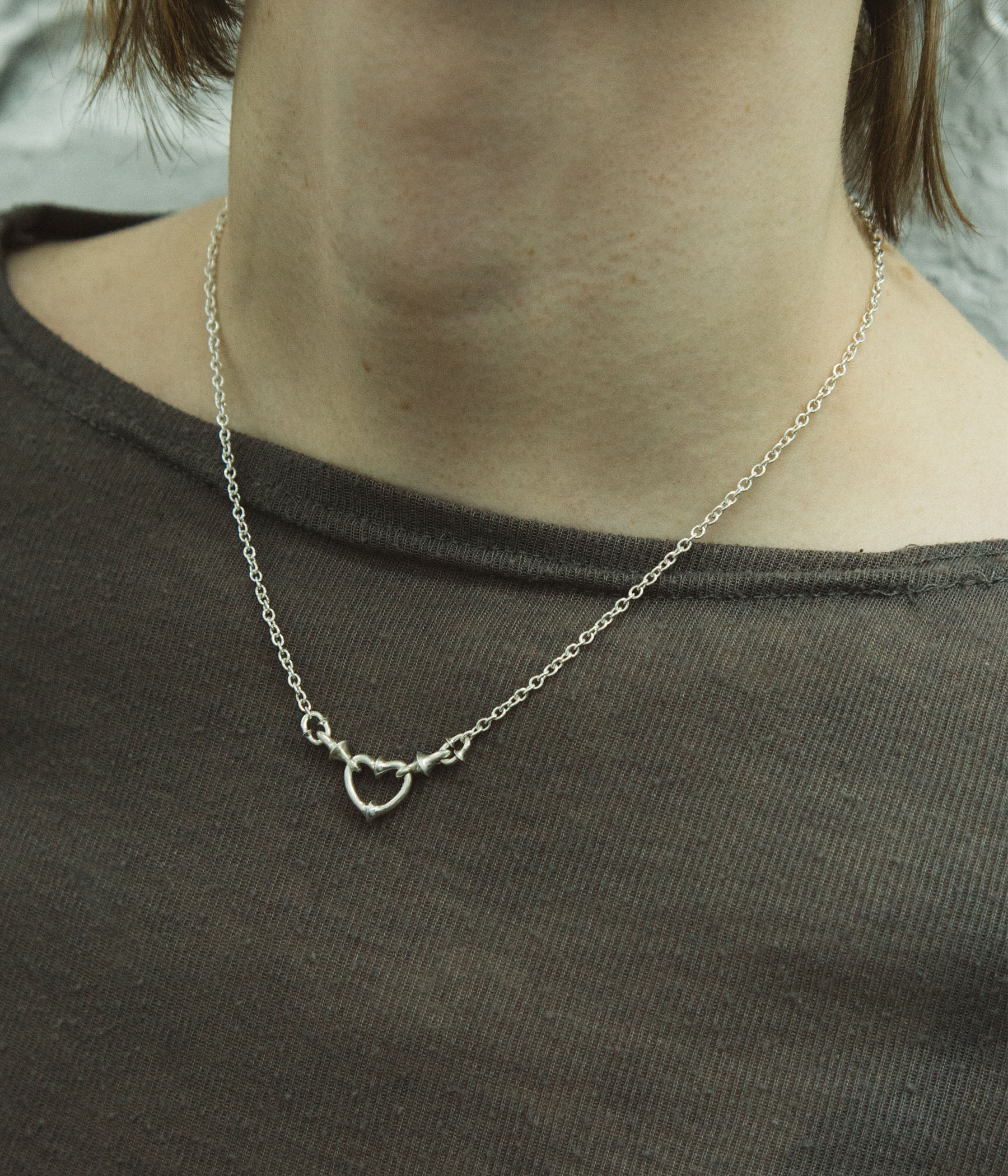 Silver necklace with a heart pendant worn by a person on a plain background