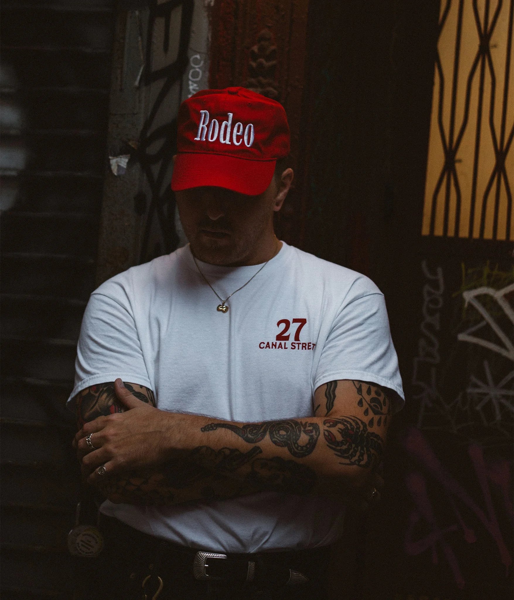 Person wearing a red 'Rodeo' cap and white t-shirt with '27 Canal Street' text, standing against a dark background.