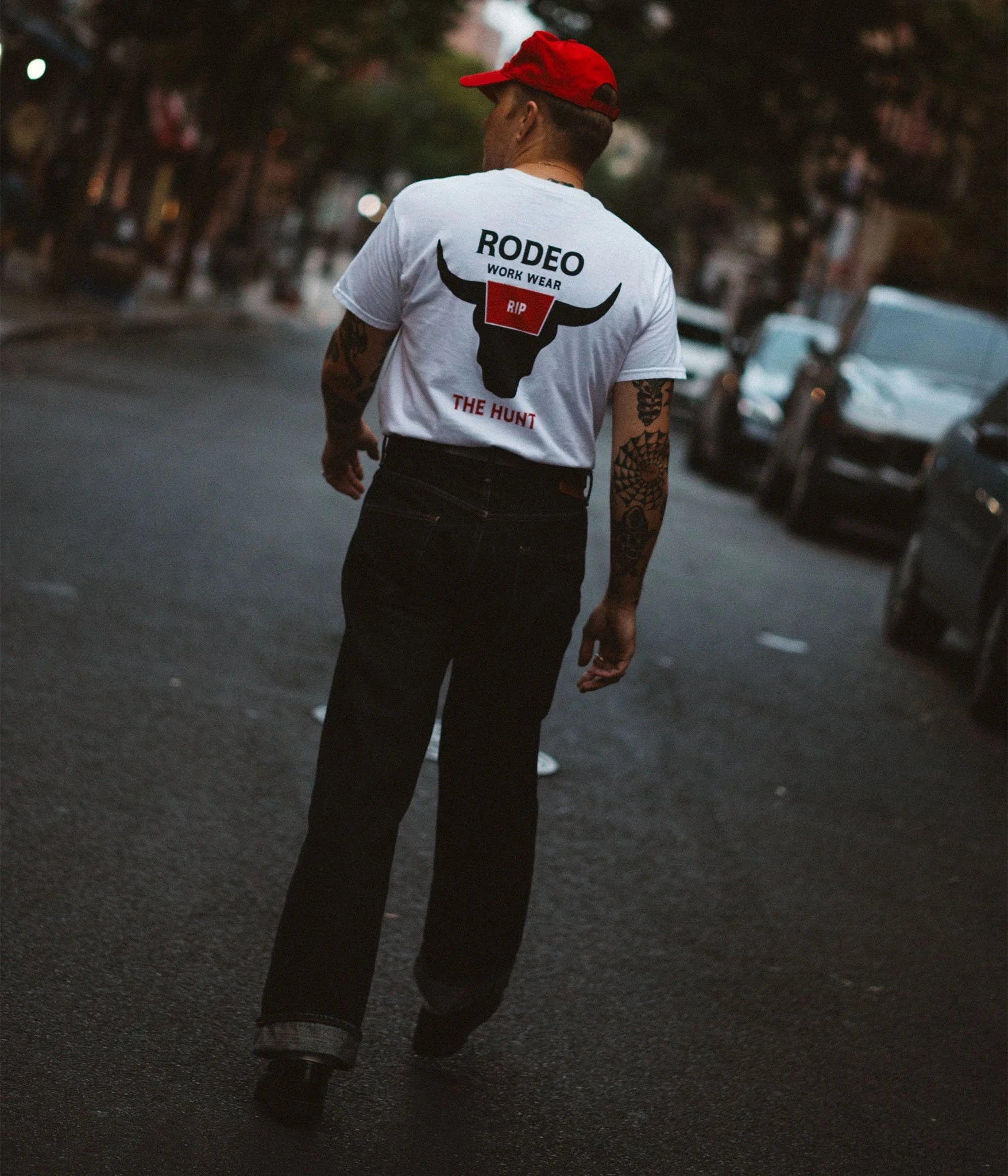 Man walking on a street wearing a white t-shirt with 'Rodeo' branding.