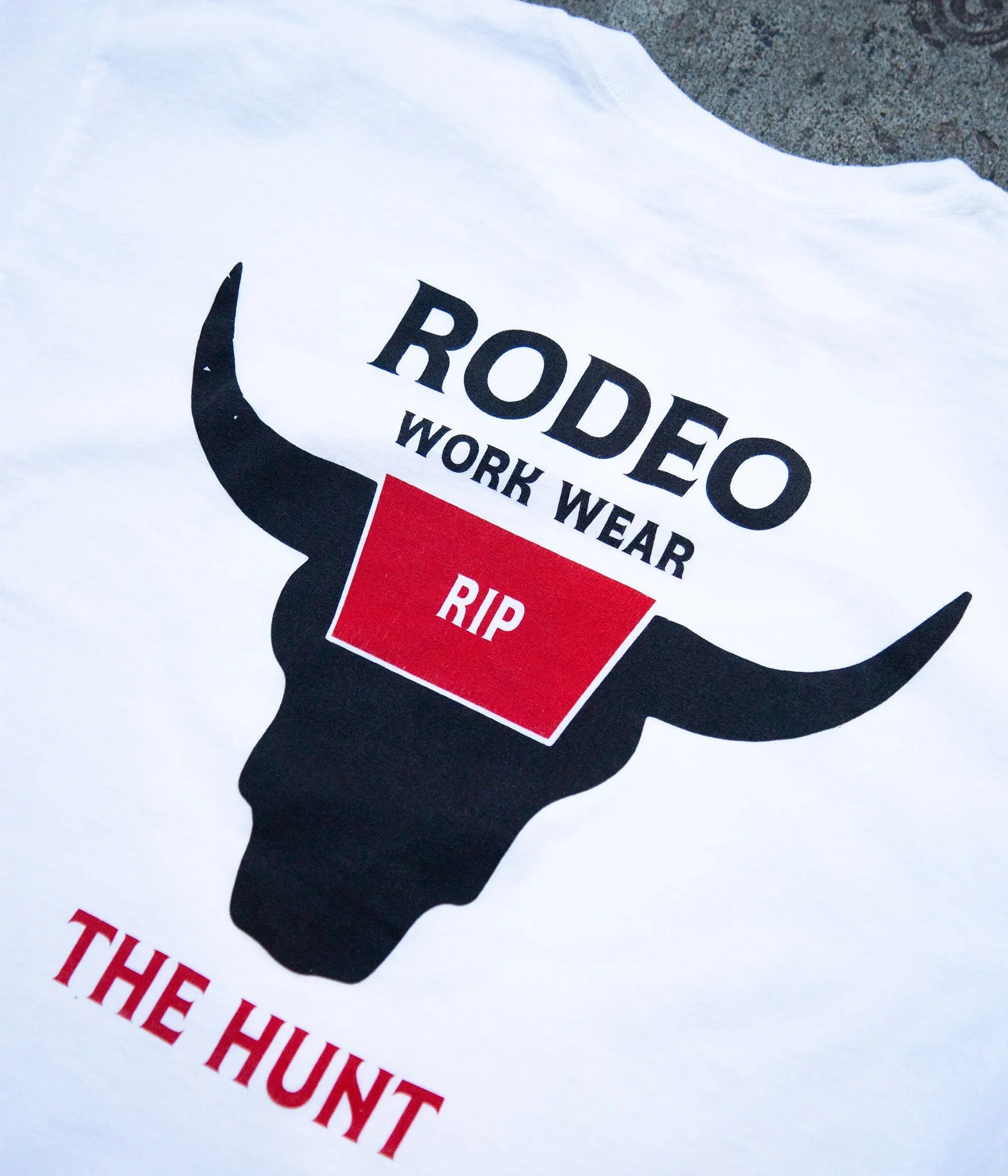White t-shirt with black bull graphic and text 'Rodeo Work Wear Rip The Hunt' on a white background.