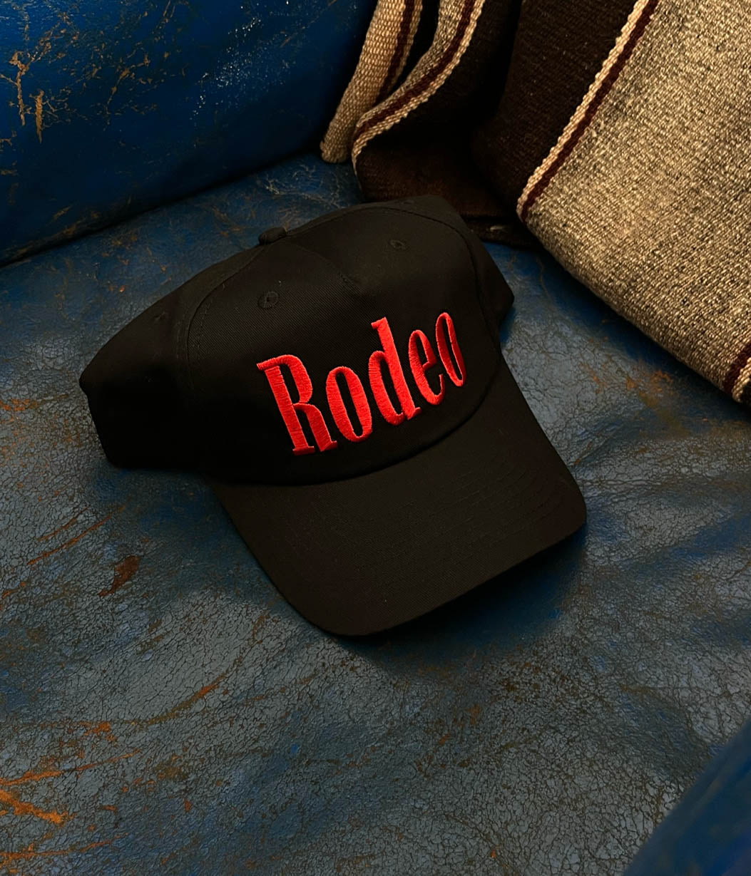 Black cap with red 'Rodeo' text on a textured blue surface