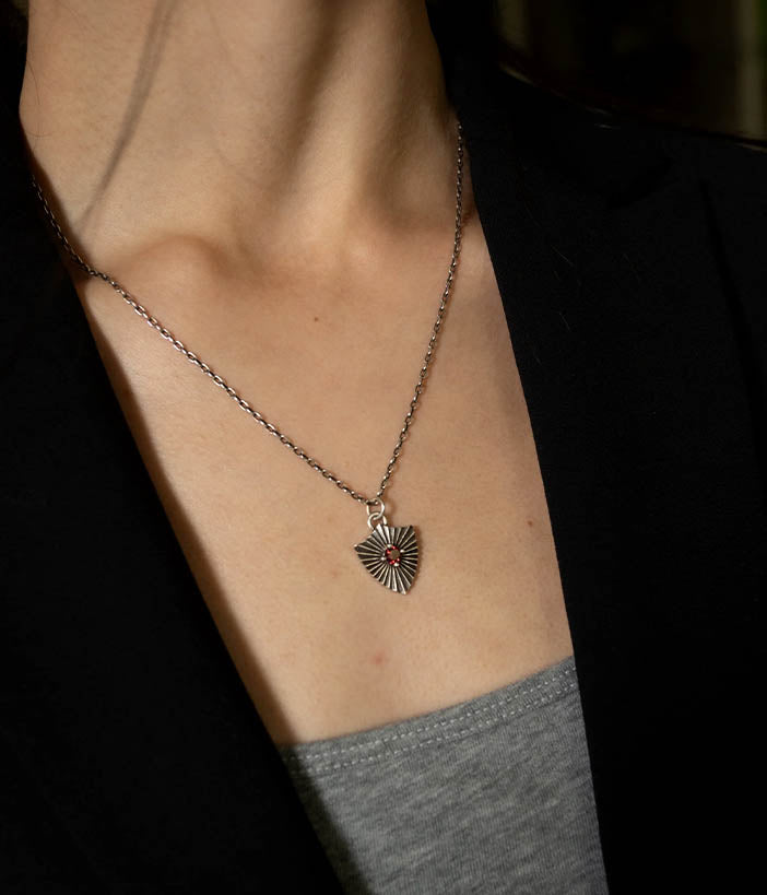 Necklace with a heart-shaped pendant on a person's arm against a dark background