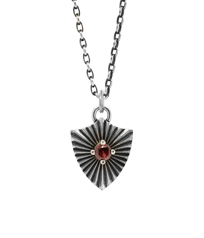 Silver necklace with a starburst pendant featuring a red gemstone on a white background